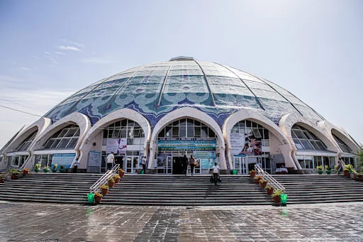 Traders and shoppers under the blue dome of Chorsu market in old Tashkent, stalls stacked with dried fruit and spices.