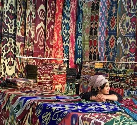 Lengths of tie-dyed ikat silk hanging in a Margilan workshop, the pattern edges deliberately blurred.