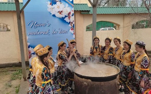 Women taking turns at a long paddle over a communal kazan of sumalak, cooked through the night before Navruz.