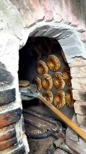 Round flatbreads stamped with a chekich, stacked warm beside a clay tandir oven.