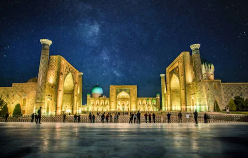 Three madrasah façades on Registan Square in Samarkand, their tiled portals lit by low evening sun.