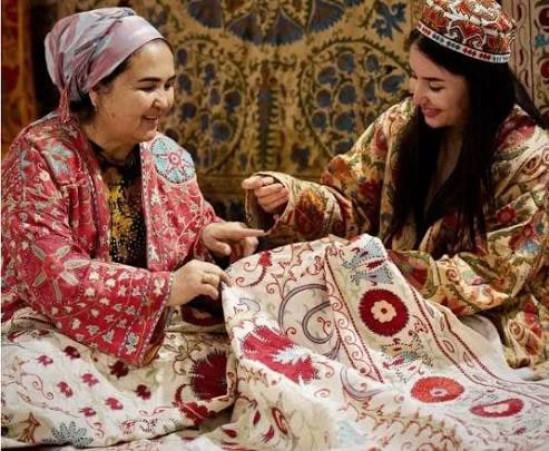 Hands working a silk-thread rosette onto cotton ground, part of an unfinished suzani panel.